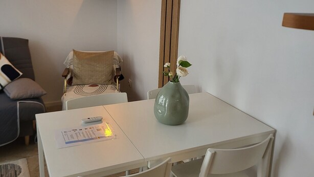 A dining area with a white table and chairs, a vase with flowers, and two wall-mounted light fixtures. - Duplex Hyper Centre-ville (Quimper)