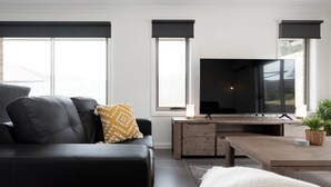 A modern living room with a black leather sofa, a wooden coffee table, and a flat-screen TV. - The Cosy Spot - with Parking (Mowbray)