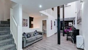 A spacious living area with a grey sofa, a staircase, and a dining area with a table and chairs. - Dukes Street Apartment Hotel (Liverpool)