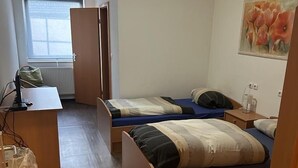 Une petite pièce bien éclairée, avec deux lits simples, un bureau et un radiateur.