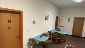 Une chambre d’hôtel avec une porte en bois portant le numéro « 12 », un coin repas avec des tables et des chaises, et un tableau blanc fixé au mur.