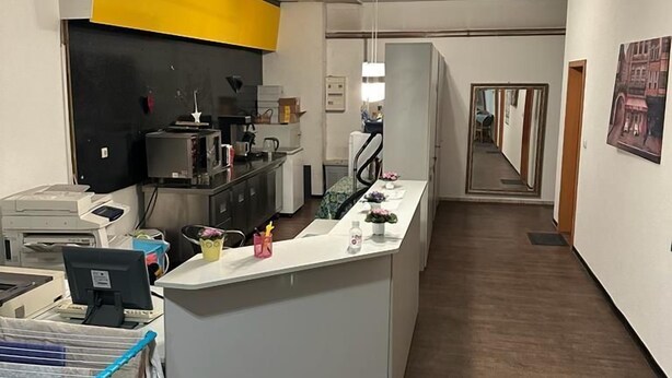 Une cuisine moderne dotée d’un îlot central, un coin repas avec une longue table, et un couloir menant à une autre pièce.