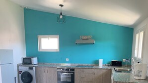 Eine moderne Küche mit Waschmaschine, Backofen und Mikrowelle, ein Essbereich mit Tisch und Stühlen sowie eine Wand in Türkis.