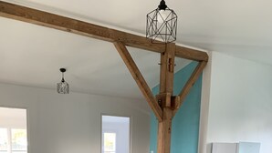 Ein modernes Wohnzimmer mit einem Holzesstisch, einer grauen Couch und einer Küchenzeile inklusive weißem Kühlschrank.