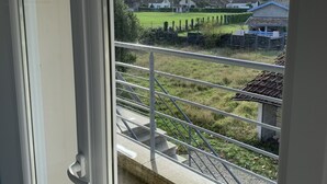 Ein Balkon mit Blick auf ein grünes Feld, ein kleines Gebäude mit blauem Dach und eine Zäunung.
