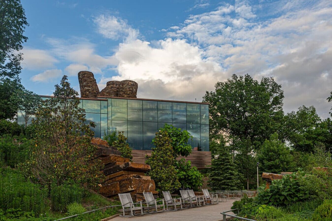 A modern building with a glass facade, surrounded by greenery and stone structures.