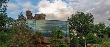 A modern building with a glass facade, surrounded by greenery and stone structures.