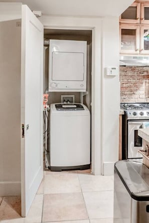 Cozinha compacta com máquina de lavar e secar integradas, fogão e painel de ladrilho.