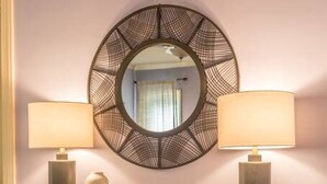 Quarto com escrivaninha de madeira, duas luminárias, um espelho e dois pufes.