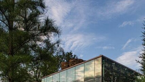 Um edifício moderno de vidro com um deck de madeira, cercado por vegetação exuberante.
