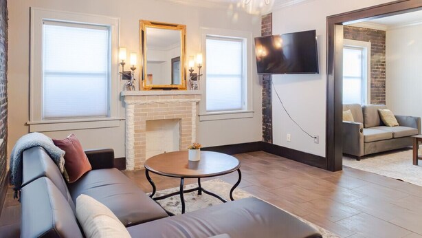 Un salon moderne avec un canapé en cuir, une table basse ronde, une cheminée et un téléviseur à écran plat fixé au mur.