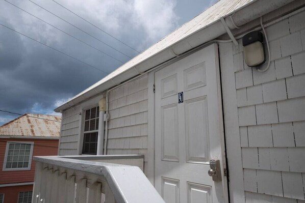 A white building with a door marked with the number 4, a window, and a metal vent on the wall.