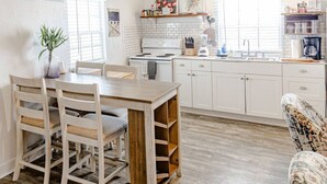 A kitchen with white cabinets, a stove, and a sink. There is a dining table with chairs and a potted plant. - Blackbeard`s Rendezvous - Downtown Danish Villa (Christiansted)
