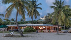 A beachfront restaurant with outdoor seating, palm trees, and a covered area. - Blackbeard`s Rendezvous - Downtown Danish Villa (Christiansted)