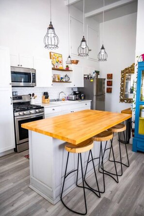 A modern kitchen with a wooden island, bar stools, a microwave, stove, and hanging pendant lights. - The Royal Wait - An Elegant Retreat (Christiansted)