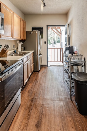 A kitchen with wooden cabinets, stainless steel appliances, a wooden floor, and a view through an open door. - Trailside Retreat in the City (Tulsa)