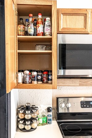 A kitchen with a wooden cabinet containing various condiments and spices. - Trailside Retreat in the City (Tulsa)