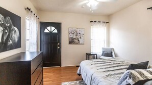 A bedroom with a bed, a dresser, a door, and a painting on the wall. - Trailside Retreat in the City (Tulsa)