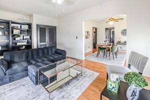 A living room with a sectional sofa, a glass coffee table, and a dining area with a table and chairs. - Trailside Retreat in the City (Tulsa)