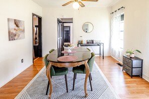 A dining area with a round table, green upholstered chairs, and a rug. There is a small side table with a plant and a mirror on the wall. - Trailside Retreat in the City (Tulsa)