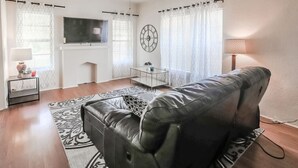 A living room with a leather sofa, a TV, a clock, and a lamp. - Trailside Retreat in the City (Tulsa)