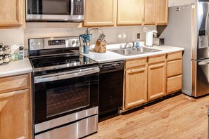 A modern kitchen with stainless steel appliances, wooden cabinets, and a dishwasher. - Trailside Retreat in the City (Tulsa)