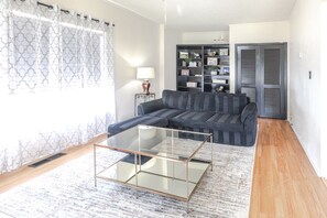 A living room with a sofa, a glass coffee table, a patterned rug, a bookshelf, and a door with shutters. - Trailside Retreat in the City (Tulsa)