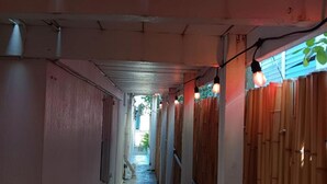 Un pasillo estrecho con paredes de madera y suelo de concreto, que conduce a un espacio abierto con plantas.