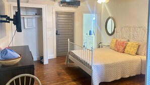 Un dormitorio con cama, ventilador de techo, televisor montado en la pared y piso de madera.