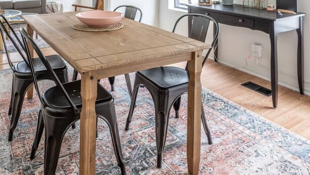 Un comedor con una mesa de madera, sillas negras y un cuenco rosa.
