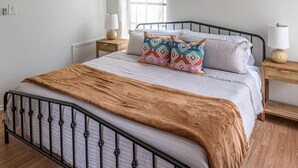 Un dormitorio con cama, mesita de noche, lámpara y ventana.