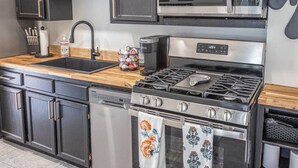 Una cocina moderna con armarios oscuros, electrodomésticos de acero inoxidable, encimera de madera y estufa a la vista.