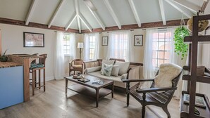 A spacious living room with a high ceiling, wooden beams, a sofa set, a coffee table, and a dining area with a blue table and wooden chairs.