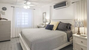 Una camera da letto con un letto, comodini, una cassettiera, una ventola a soffitto e una finestra con tende.