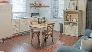A kitchen with wooden cabinets, a dining table with chairs, a ceiling fan, and a blue sofa in a living area. - The Rooster’s Perch - A Quaint Island Homestead (Christiansted)