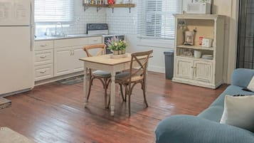 Une cuisine avec des meubles en bois, une table à manger avec des chaises, un ventilateur de plafond et un canapé bleu dans l’espace salon.