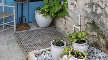 Une porte bleue portant l’inscription « DOUCHE », une chaise blanche et des plantes en pot dans une cour.