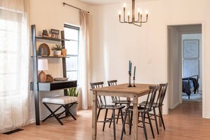 A dining area with a wooden table and chairs, a chandelier, and a shelf with decorative items. - Hermes` Respite - A Runner`s Paradise (Tulsa)