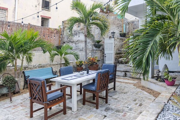 An outdoor patio with a table and chairs, surrounded by potted plants and a stone wall.