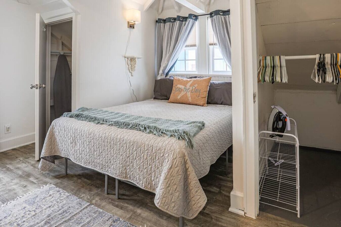 A bedroom with a bed, a nightstand, a wall-mounted lamp, a window with curtains, and a radiator.
