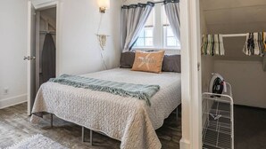 Un dormitorio con cama, mesita de noche, lámpara de pared, ventana con cortinas y radiador.