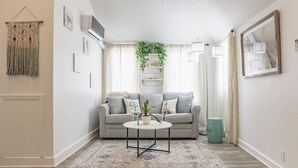Una sala de estar con un sofá gris, una mesa de centro redonda, un tapete estampado y un cubo de basura verde.