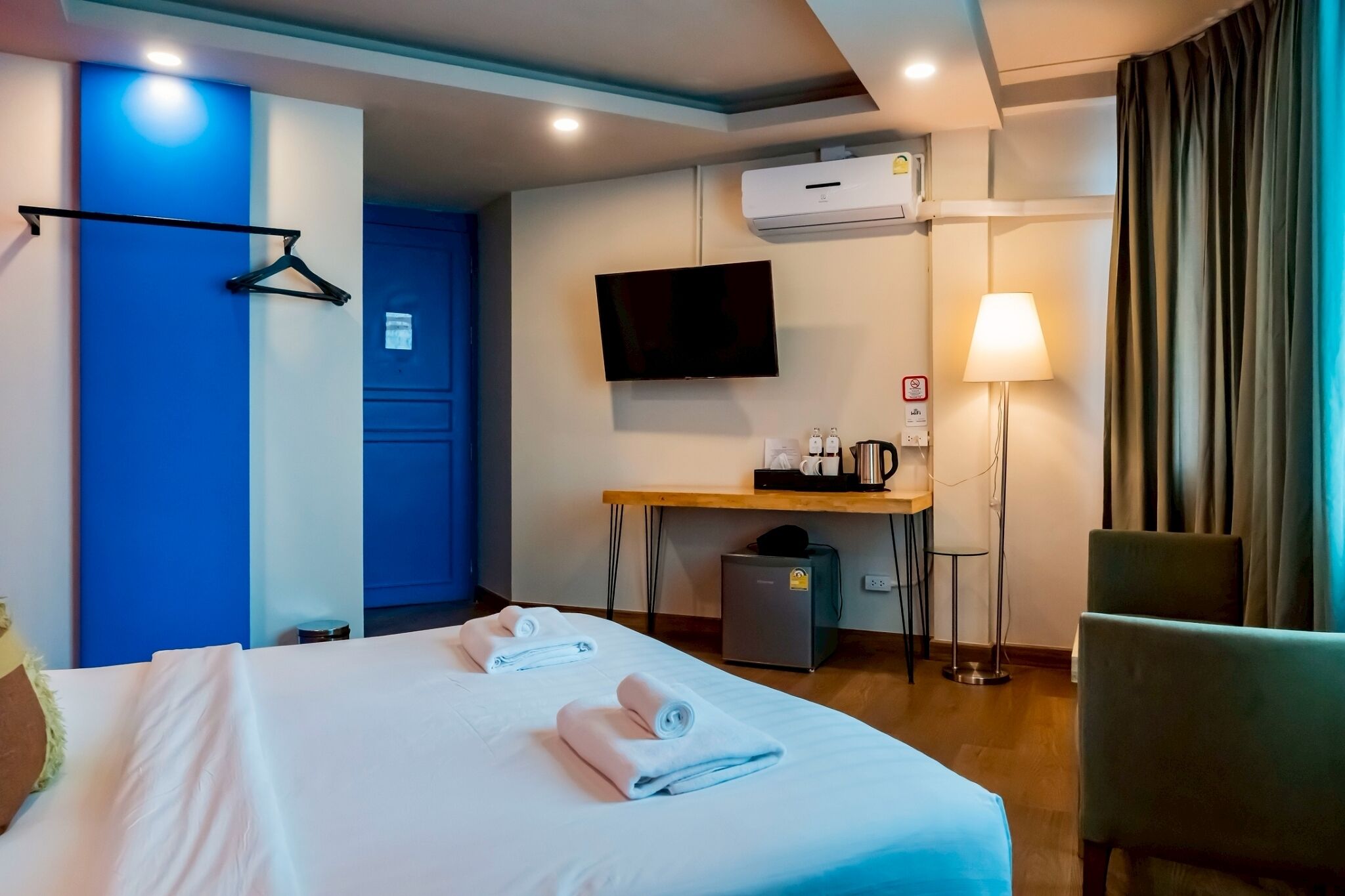 A hotel room with a bed, a desk with a flat-screen TV, a coffee maker, a lamp, and a chair.