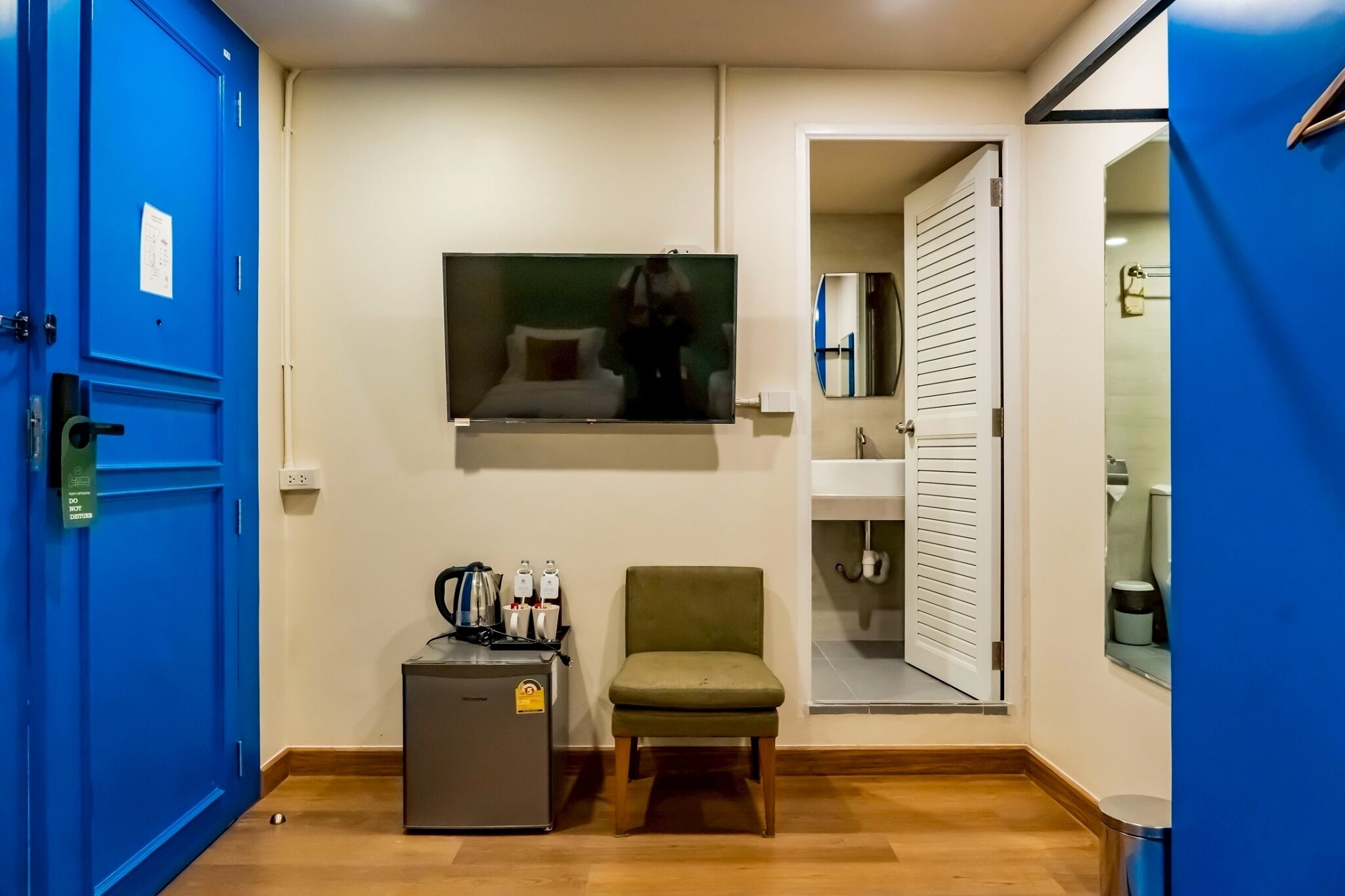 A compact room with a bed, a small refrigerator, a chair, and a television mounted on the wall.