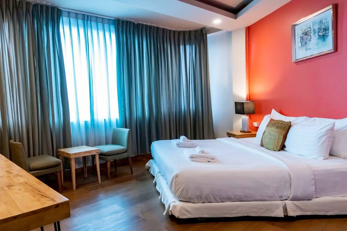 Una habitación de hotel con una cama grande, una mesita pequeña, una silla y un escritorio.