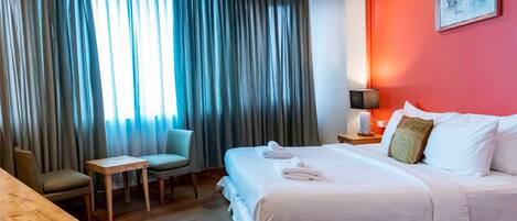 A hotel room with a large bed, a small table, a chair, and a desk.