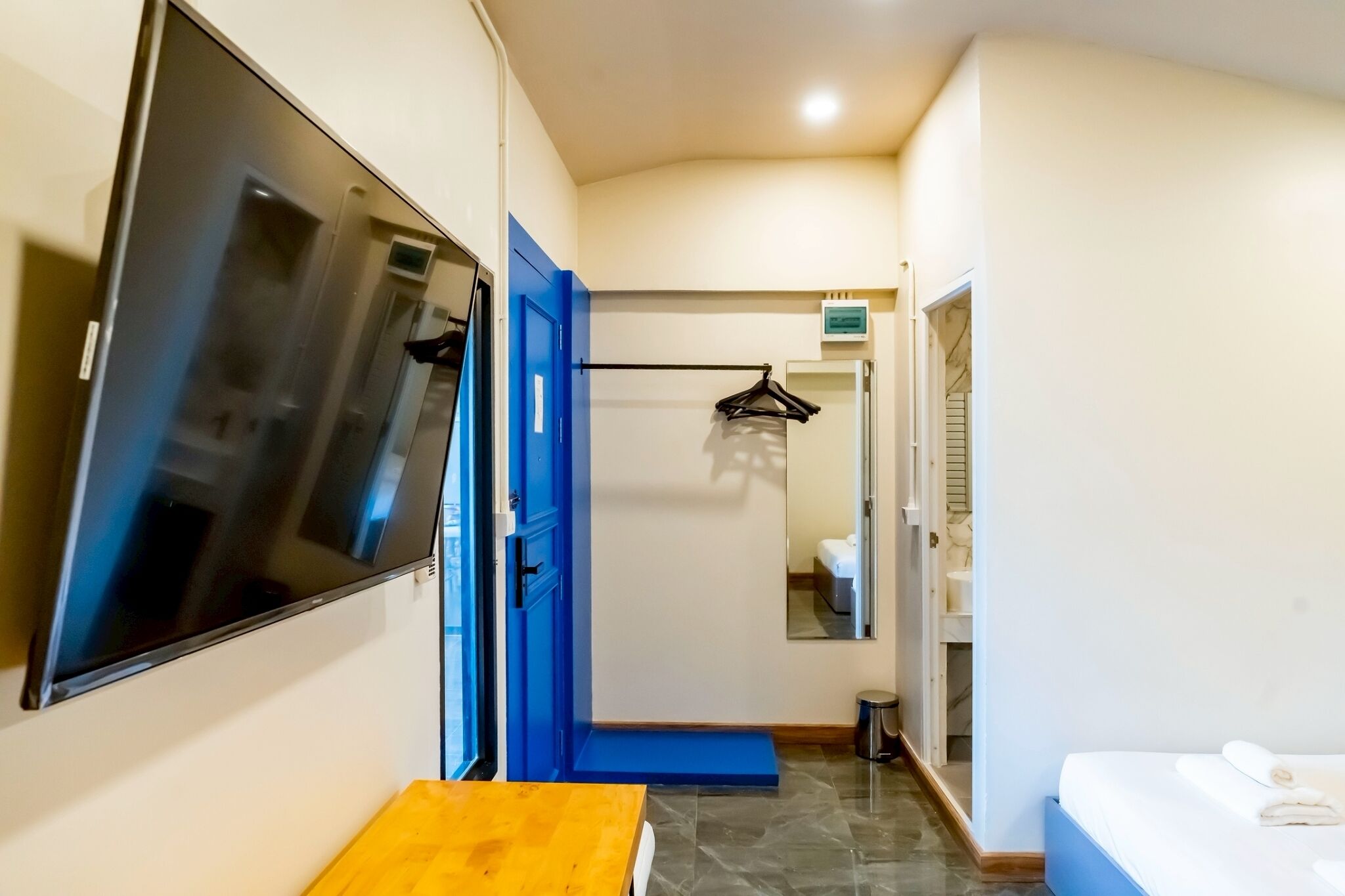 A hotel room with a large mirror, a bed with a white comforter, a wooden bench, and a blue door.
