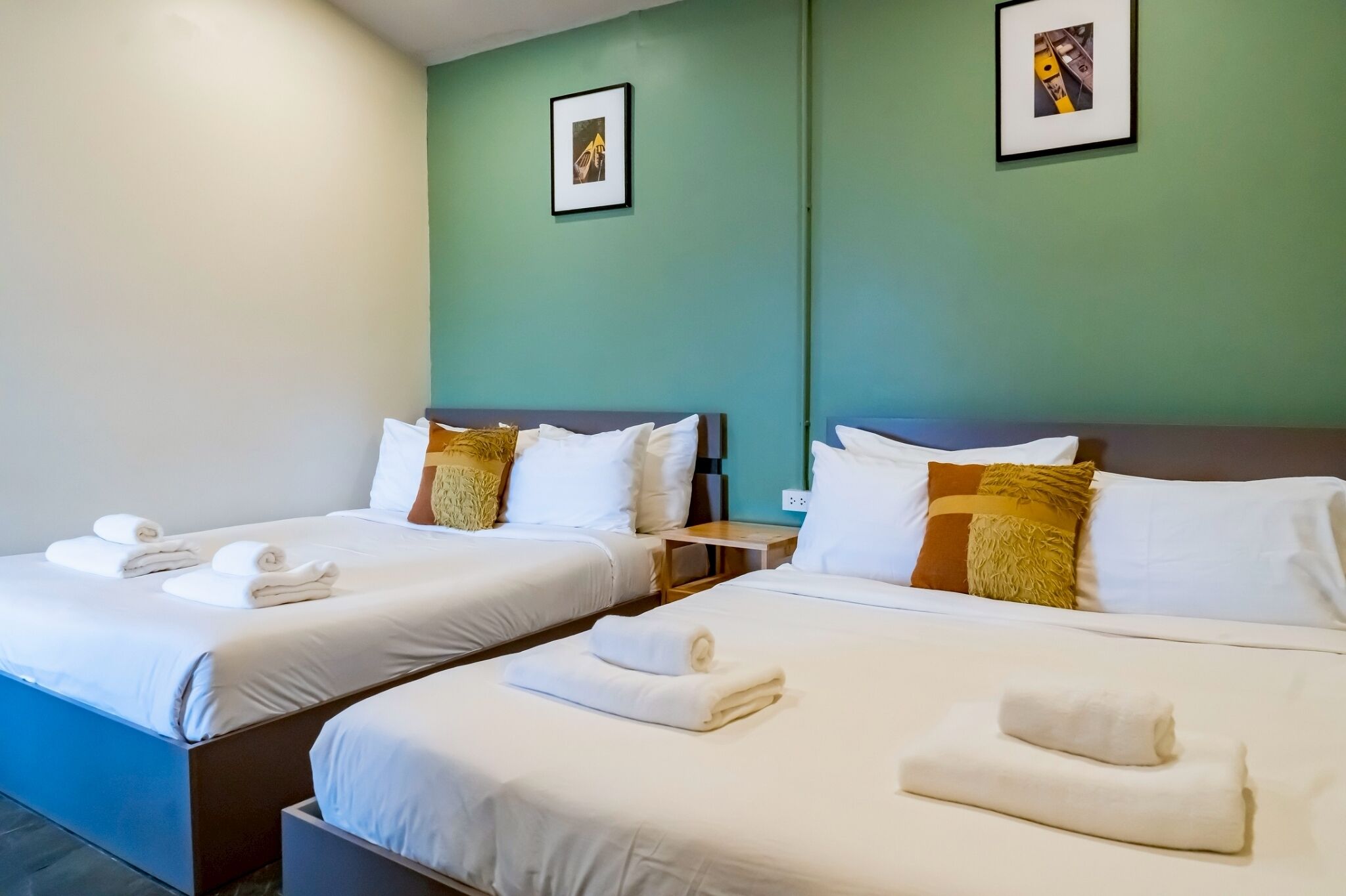 Two twin beds with white linens and towels, a green wall, and framed pictures.