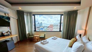 Ein Hotelzimmer mit einem gro ßen Bett, einem Schreibtisch mit Stuhl, einem Fernseher und einem Fenster mit Vorhängen.