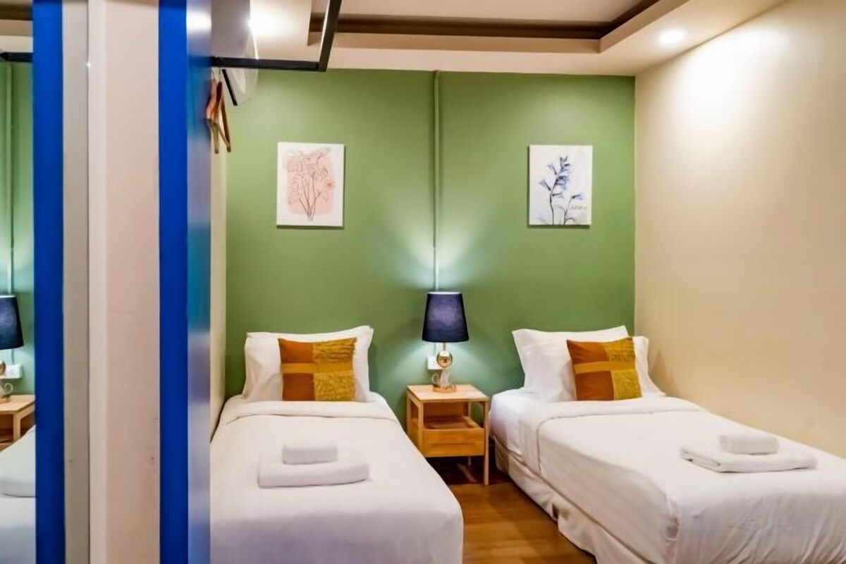 A hotel room with two single beds, a nightstand with a lamp, and artwork on the walls.